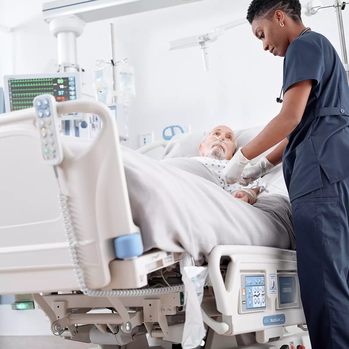 Female Nurse administering medication to male patient in Hillrom Progressa ICU Bed