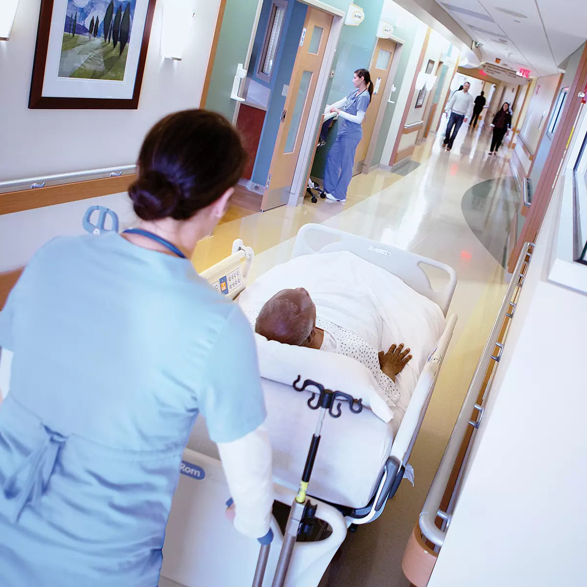 Female Nurse pushing Male Patient down hospital hallway in Hillrom Progressa ICU Bed